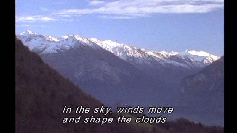 Snow-capped mountains with thin clouds above. Caption: In the sky, winds move and shape the clouds