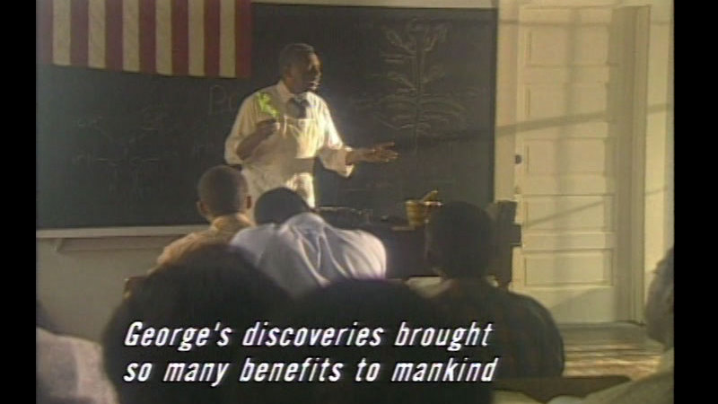Man standing at chalk board in front of class. Caption: George's discoveries brought so many benefits to mankind