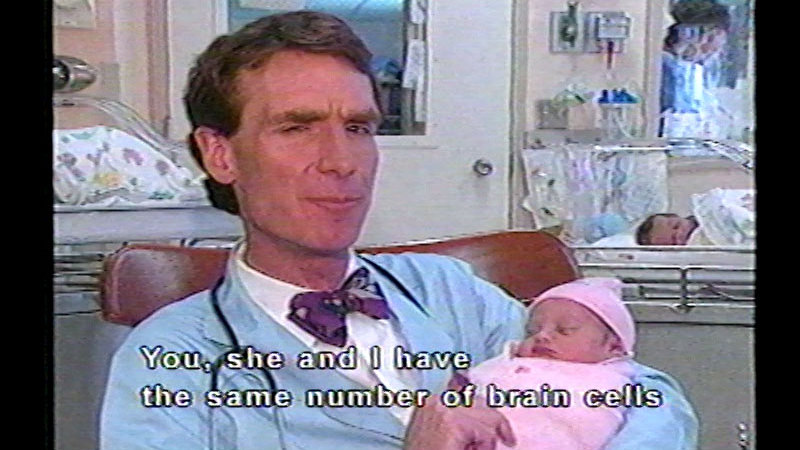 Bill Nye holding an infant. Caption: You, she, and I have the same number of brain cells
