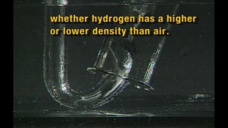 Narrow curving tube exits into a wider tube. Both are underwater. Caption: whether hydrogen has a higher or lower density than air.