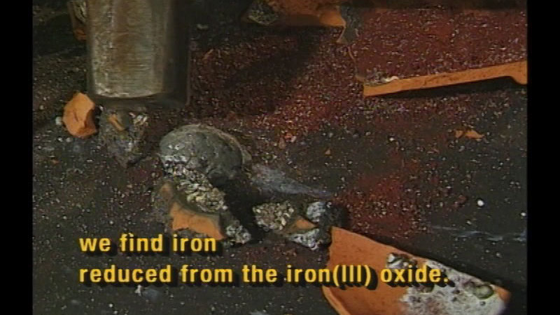 Broken pottery with a lump of metal on the ground. Caption: we find iron reduced from the iron(III) oxide.