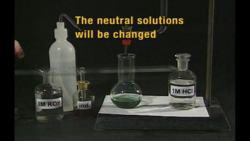 Beakers labelled 1M KOH, ind. and 1M HCI. Another beaker with a greenish liquid has a tube with a nozzle at the mouth of it. Caption: The neutral solutions will be changed