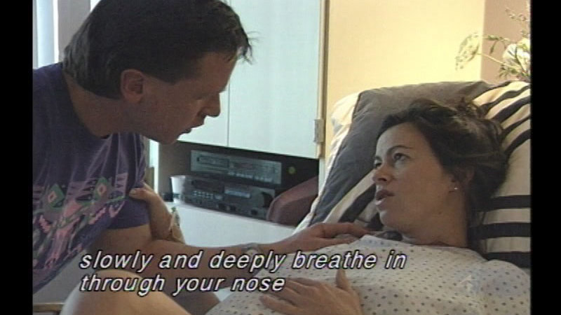 Pregnant woman lying in bed with a person leaning over and talking to her. Caption: slowly and deeply breathe in through your nose