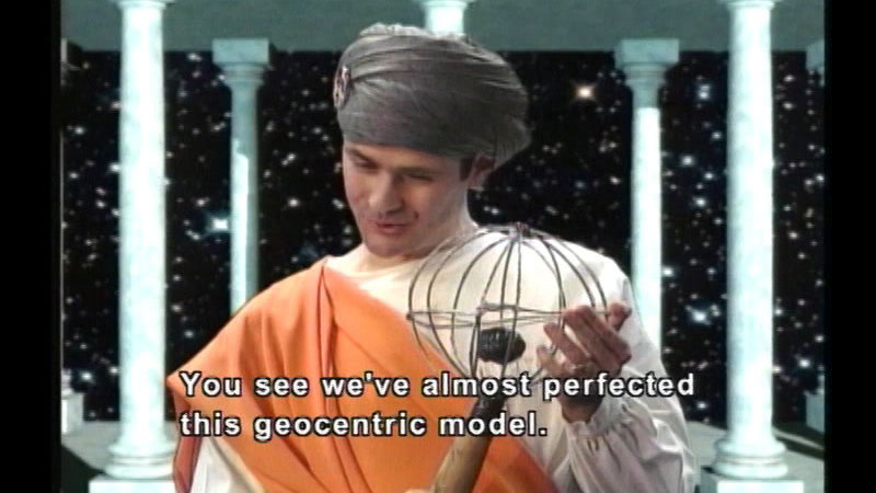 Person in a toga and head dress holding a spherical object with a round object in the center. Caption: You see we've almost perfected this geocentric model.