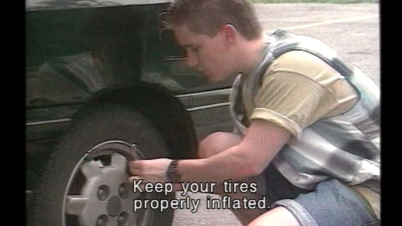 Person crouching and checking the air pressure on the tire of a vehicle. Caption: Keep your tires properly inflated.