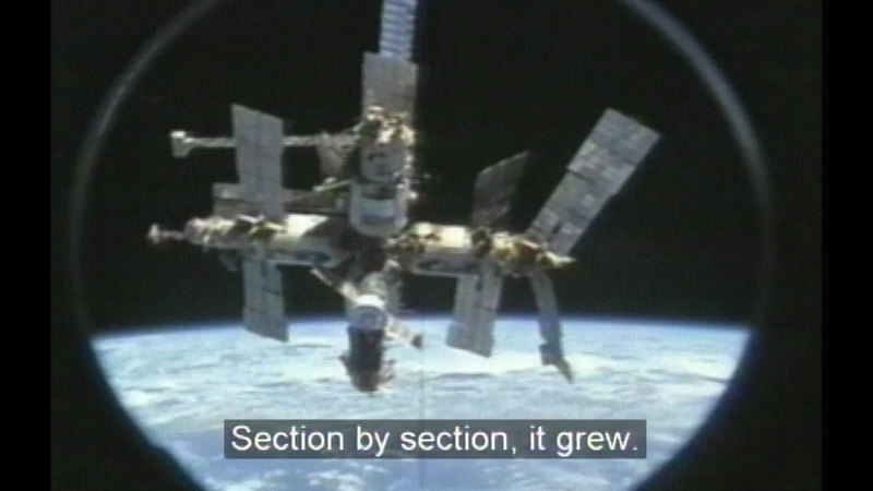 Space station as seen from space. Caption: Section by section, it grew.