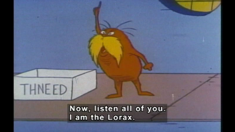The Lorax with arm raised and finger pointing upwards. Next to him on the ground is a box that says "Thneed". Caption: Now, Listen all of you. I am the Lorax.