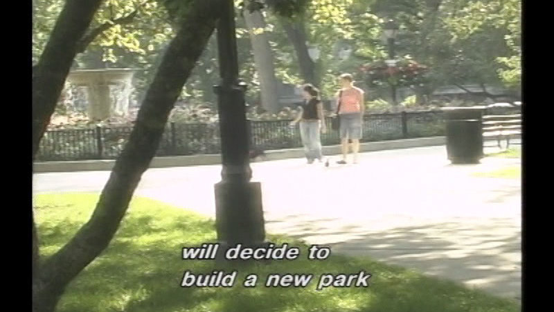 Two people walking on a paved path through a park. Caption: will decide to build a new park