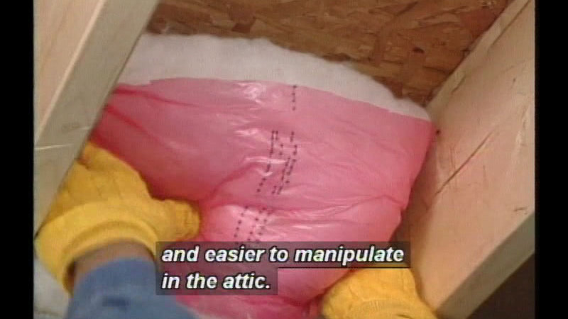 Gloved hands placing insulation in between ceiling beams. Caption: and easier to manipulate in the attic.