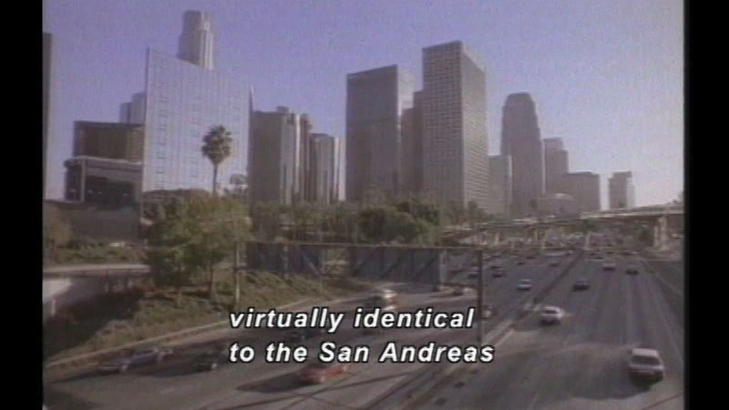 Busy freeway with palm trees and high-rise buildings in the background. Caption: virtually identical to the San Andreas