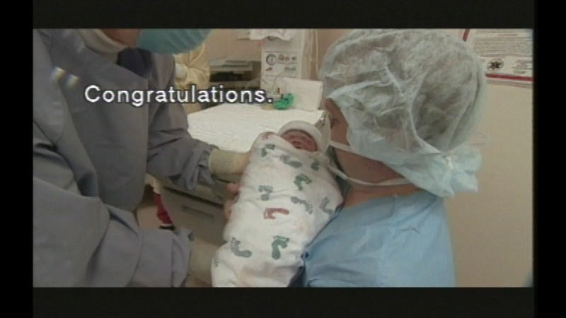 People wearing hospital gowns and masks holding a newborn baby. Caption: Congratulations.