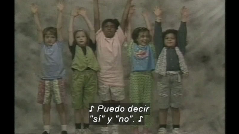 Group of children with arms raised. Spanish captions.