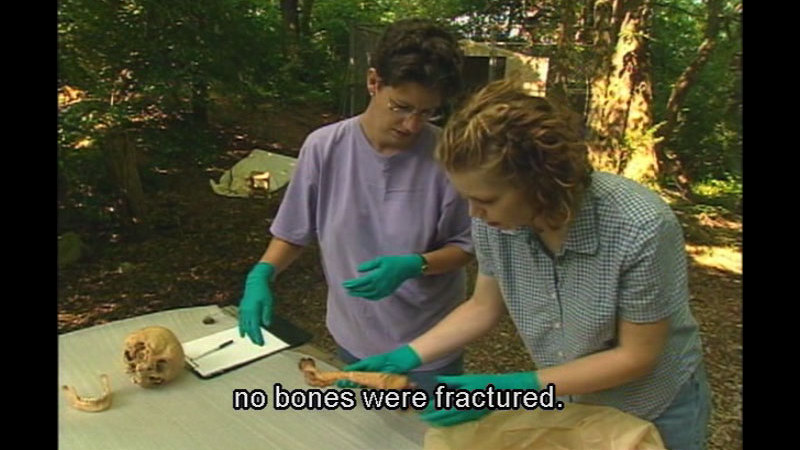 Two people wearing gloves and examining human bones. Caption: no bones were fractured.