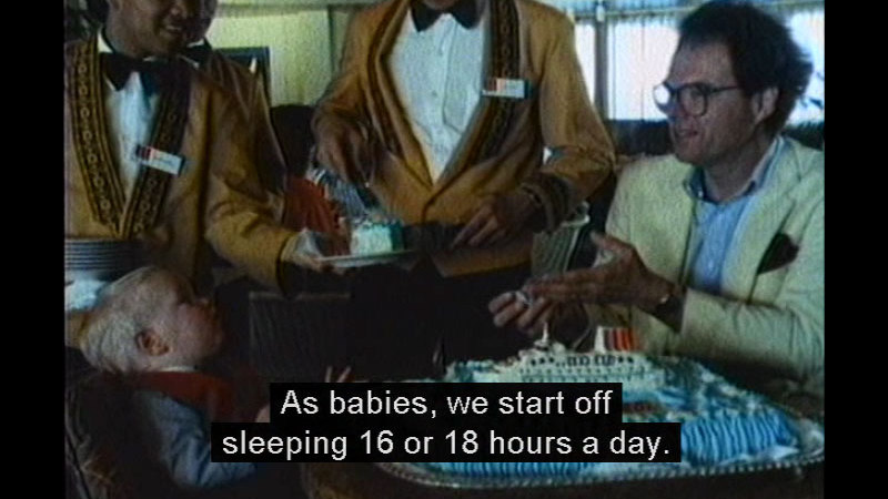 Toddler in a chair with adults at a restaurant. Caption: As babies, we start off sleeping 16 or 18 hours a day.