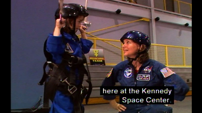 A child wearing a harness next to a woman. Caption: here at the Kennedy Space Center.