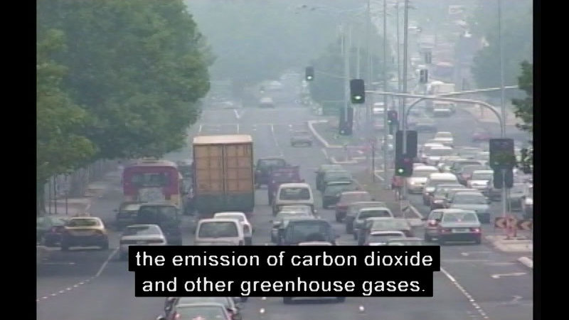 Congested city street, hazy with smog. Caption: the emission of carbon dioxide and other greenhouse gases.