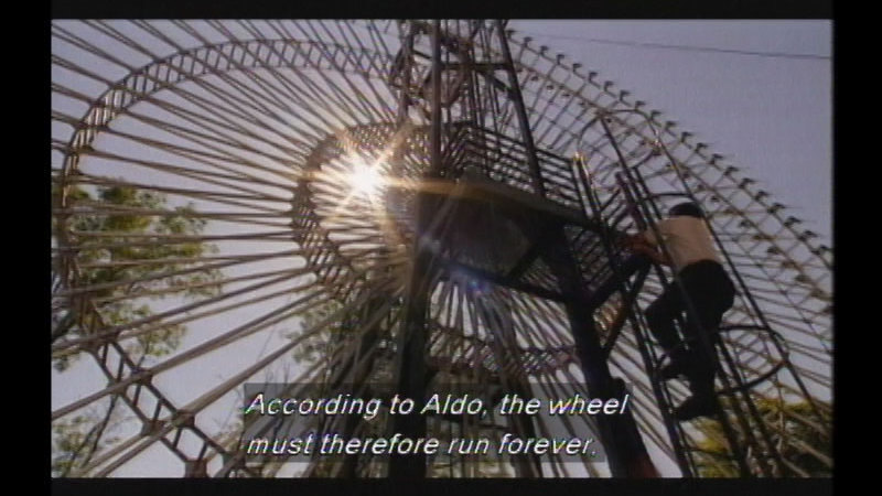 A giant stationary hollow wheel constructed of metal spokes. A person climbs up an access ladder to the center of the wheel. Caption: According to Aldo, the wheel must therefore run forever.