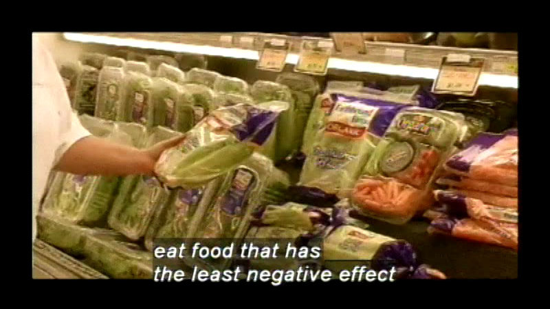 Person holding a package of lettuce while standing in front of shelves of produce. Caption: eat food that has the least negative effect