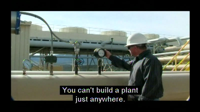 Person in a hard hat looking at a pressure gauge attached to industrial pipes. Caption: You can't build a plant just anywhere.