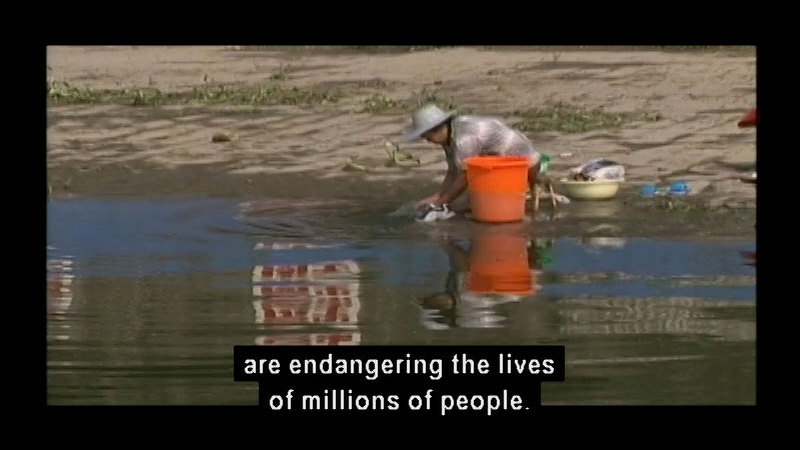 Person crouched down by the water's edge washing shoes and other items. Caption: are endangering the lives of millions of people.