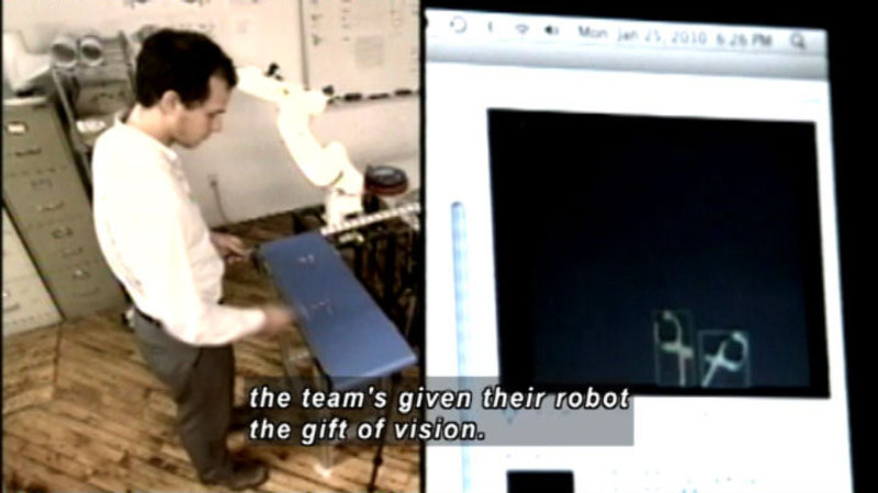 Person standing and working on something at waist level. Image of a computer screen. Caption: the team's given their robot the gift of vision.