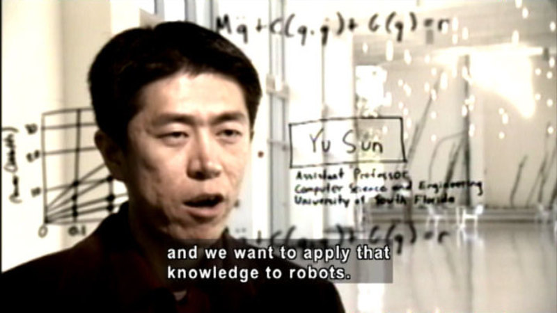 Person speaking. Behind them is a graph, mathematical equations, and writing. Caption: and we want to apply that knowledge to robots.