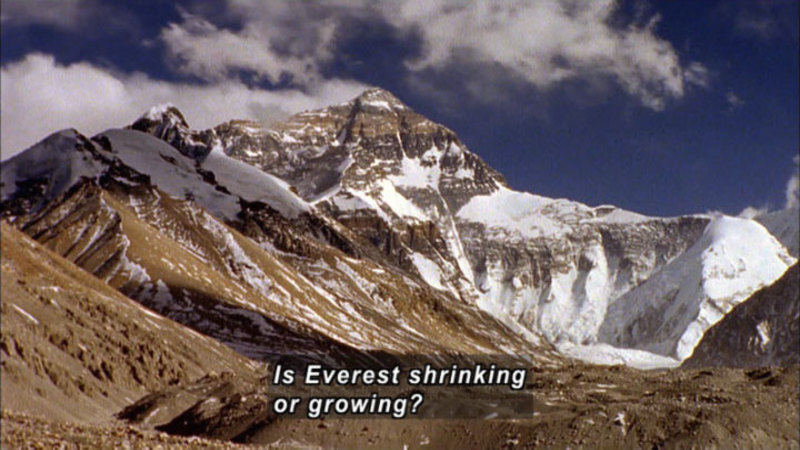 Tall, snowy, and rocky mountain as seen from below. Caption: Is Everest shrinking or growing?