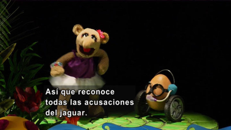 Colorful puppets on a jungle themed stage. Spanish captions.