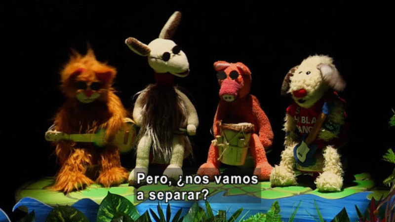 Four animal puppets playing instruments on the bank of a river. Spanish captions.