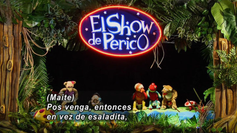 Animal puppets in front of the backdrop of a jungle. Spanish captions.