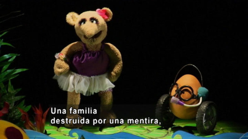 A girl puppet talking to another puppet. Spanish captions.