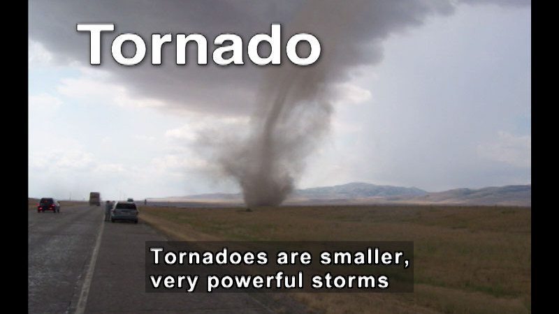 Vehicles driving on a road with a funnel-shaped cloud descending from the sky. Caption: Tornadoes are smaller, very powerful storms