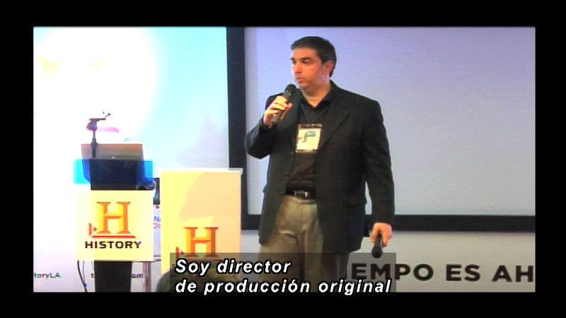 Person standing next to a podium with the History channel logo while speaking. Spanish captions.