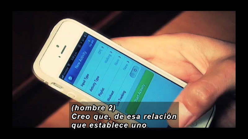 Person holding a smart phone. Spanish captions.