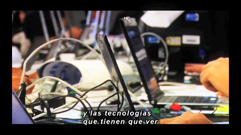 Open laptops with people working on them. Spanish captions.