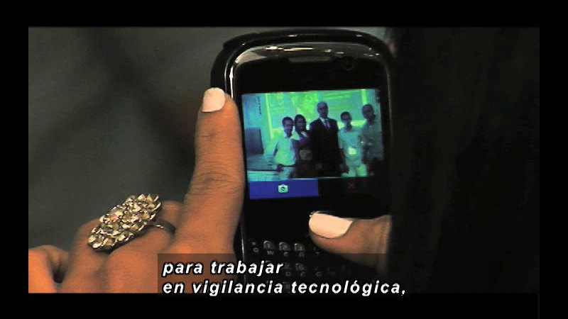Person holding a phone with a photo displayed on the screen. Spanish captions.