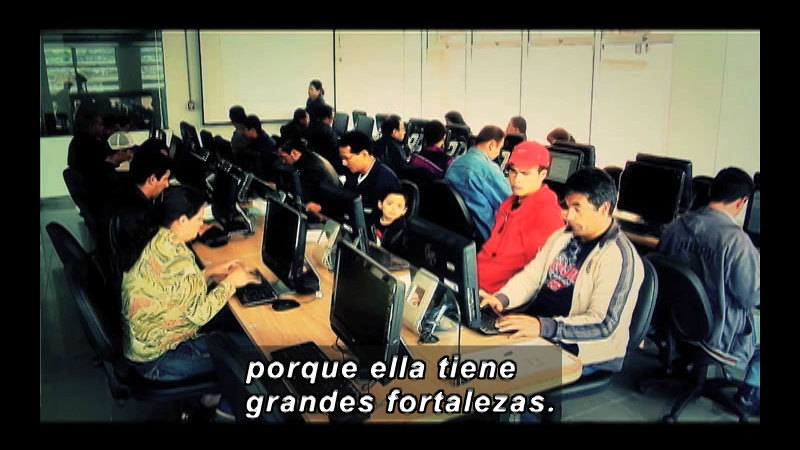 Rows of computers with people at them. Spanish captions.