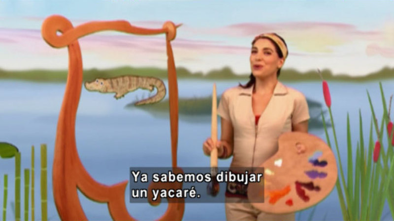 A woman with a painting pallet and a paintbrush. On her painting there is an animal that looks like an alligator. Spanish captions.