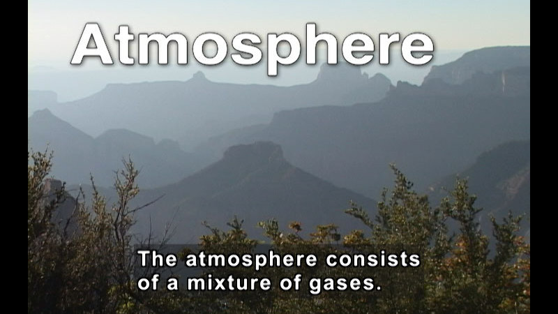Treetops in the foreground and rolling mountains in the distance. Caption: The atmosphere consists of a mixture of gases.
