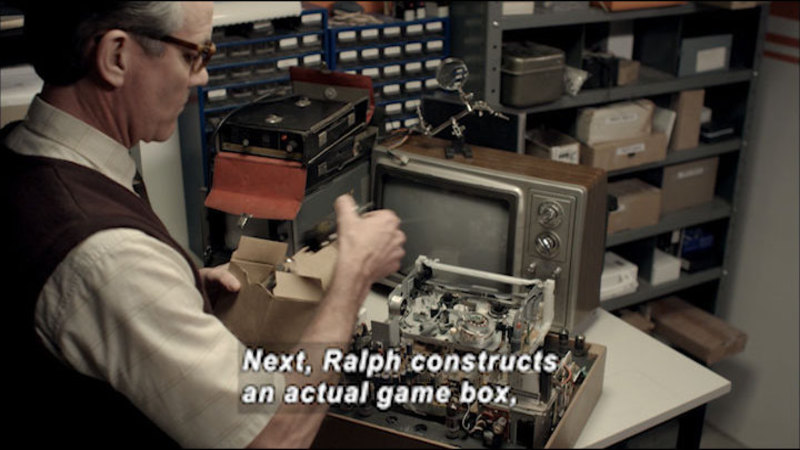 Person with a complex arrangement of wires and electronics partially assembled. Caption: Next, Ralph constructs an actual game box,