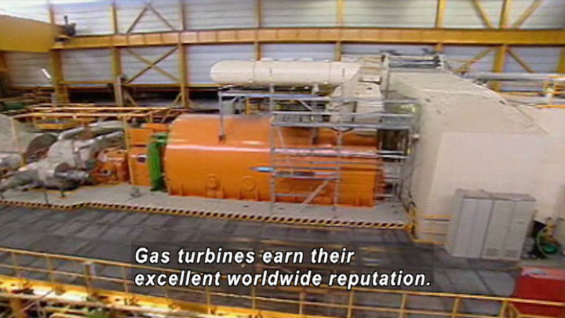 A large cylindrical machine set into the floor with various equipment attached to the round openings at either end. A walkway surrounds the mass of equipment. Caption: Gas turbines earn their excellent worldwide reputation.