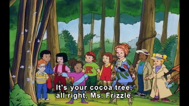 Students and their teacher from the magic school bus in standing in a jungle in front of a tree with white puffy blooms on the trunk. Caption: It's your cocoa tree, all right, Ms. Frizzle.