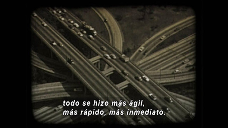Multiple levels of freeway on and off ramps with vehicles. Spanish captions.