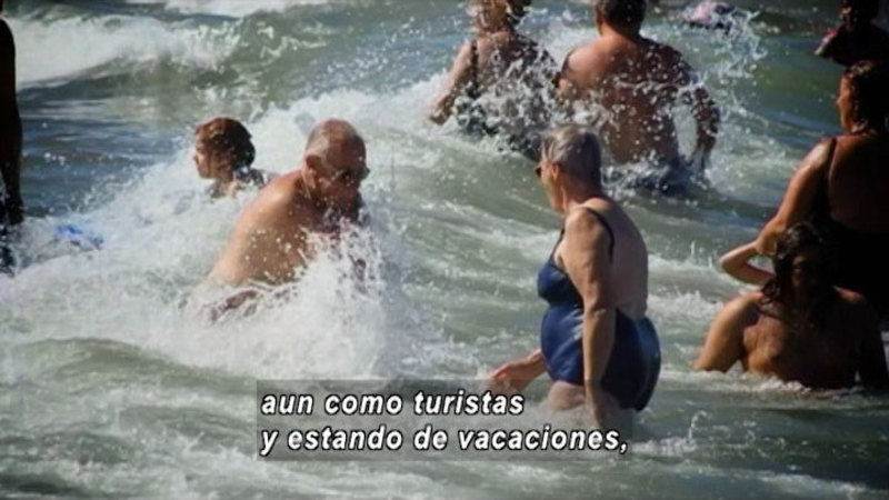 People wearing swimsuits in the ocean. Spanish captions.