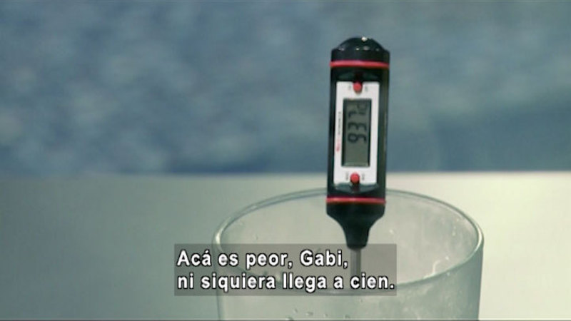 Thermometer in a glass showing a temperature of 93.7. Spanish captions.