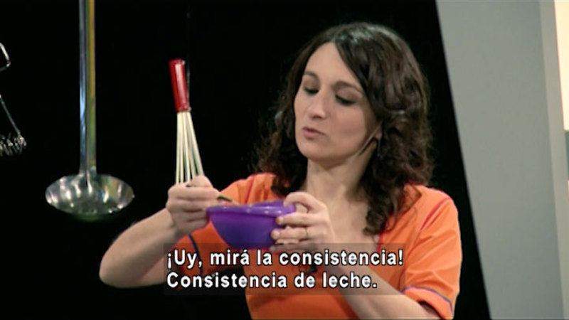 A person holds a bowl in one hand a spoon immersed in the bowl with the other hand. Spanish captions.