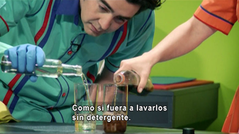 People pouring fluids from bottles into beakers. Spanish captions.