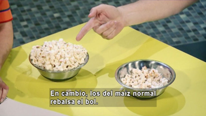Two metal bowls with popped popcorn. One bowl is overflowing, the other is half empty. Spanish captions.