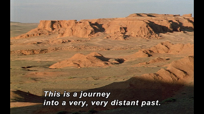 Barren, brown landscape with low, flat-topped hills. Caption: This is a journey into a very, very distant past.