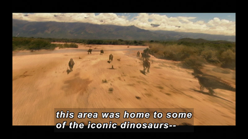 Dinosaurs running across a sandy expanse bordered by low trees. Caption: This area was home to some of the iconic dinosaurs --